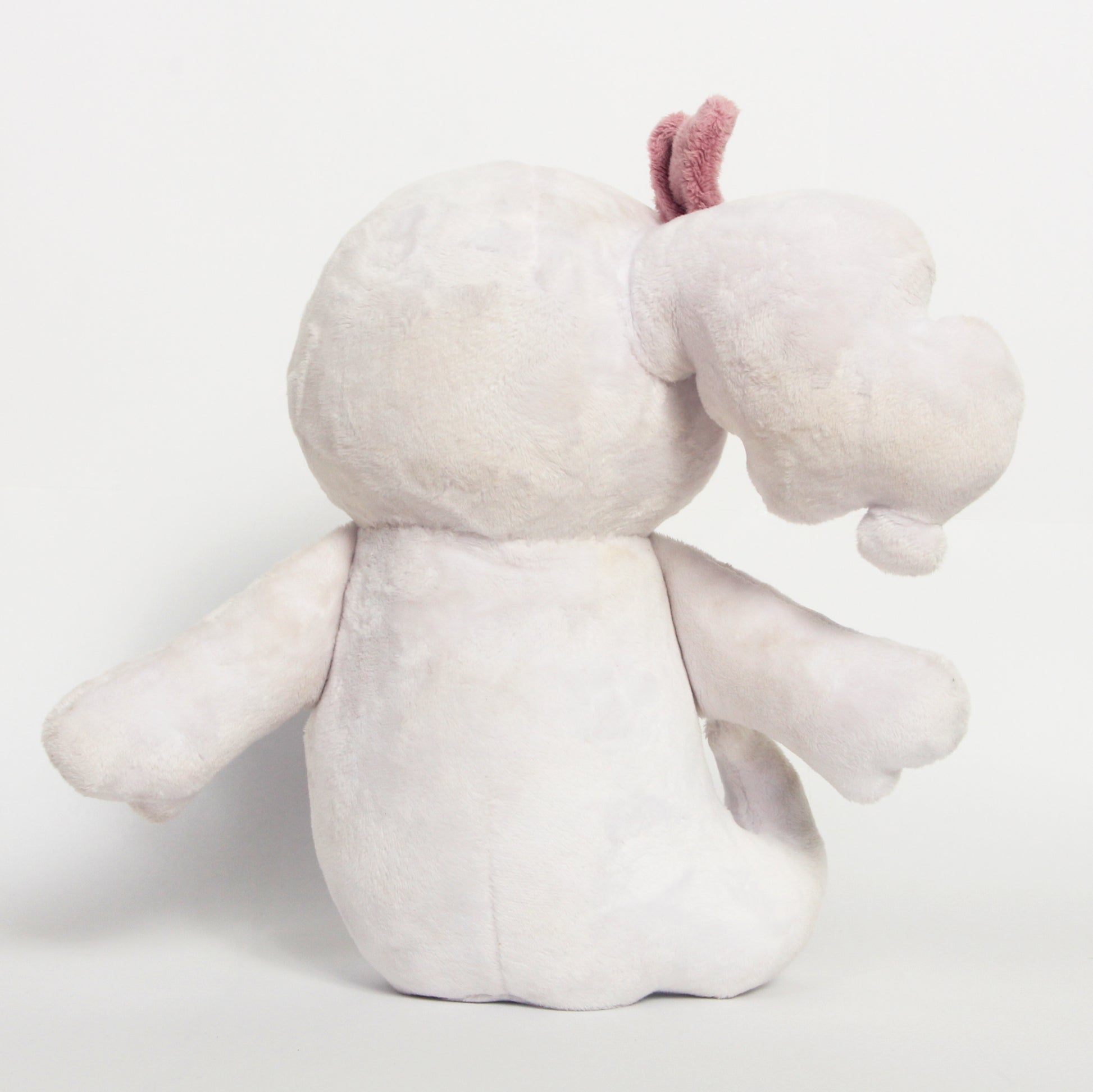 The back of a plush toy photographed against a plain light gray studio background. 